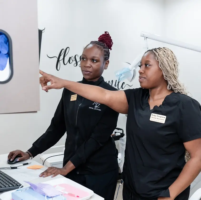 Two dental professionals, one pointing at a screen while the other uses a mouse in a dental clinic.