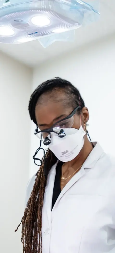 Dr. Ashlee Goodman-Tabari wearing a white coat, safety glasses with magnifiers, and a 3M face mask.
