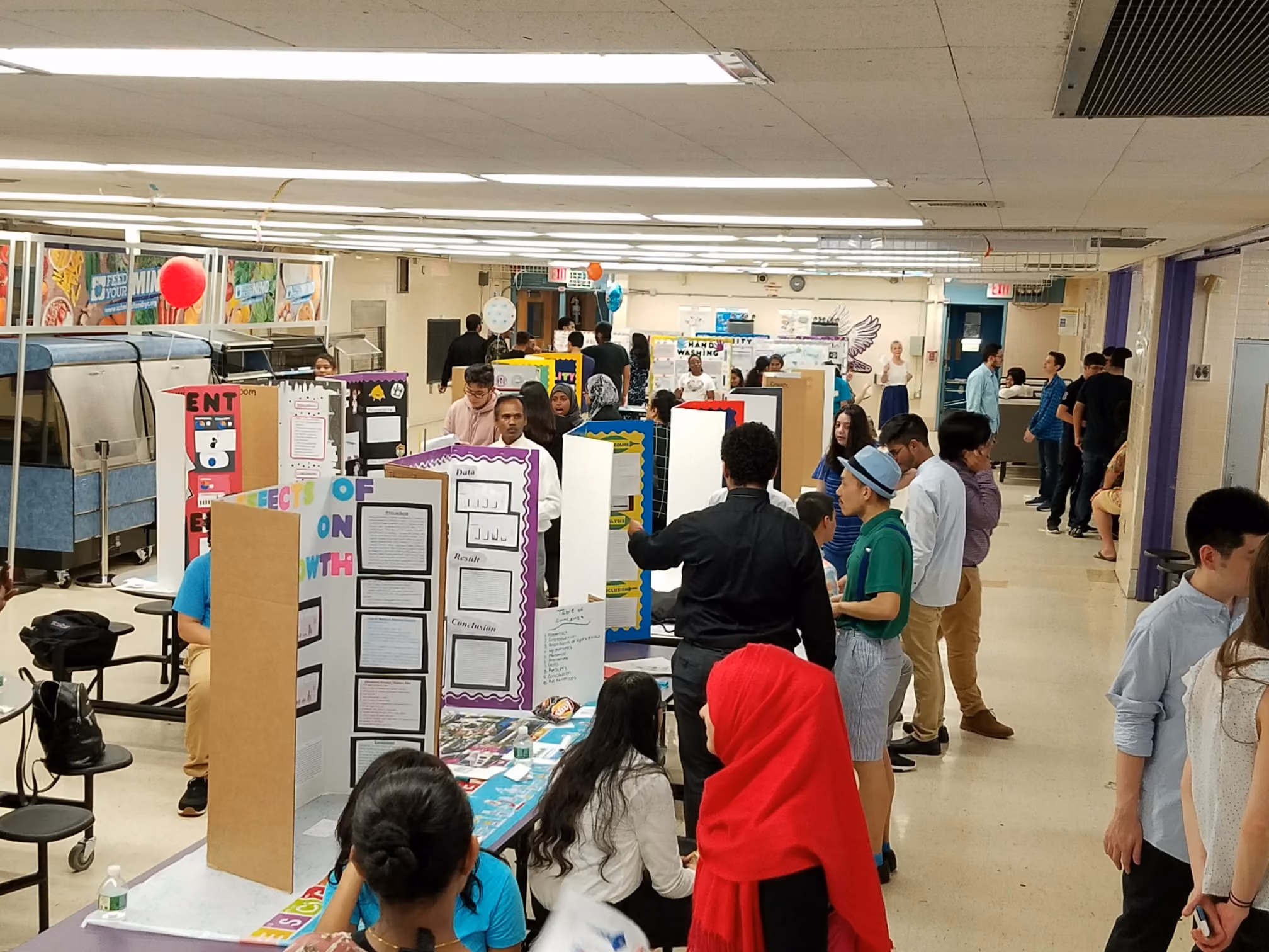Students browsing science fair project displays in school gymnasium