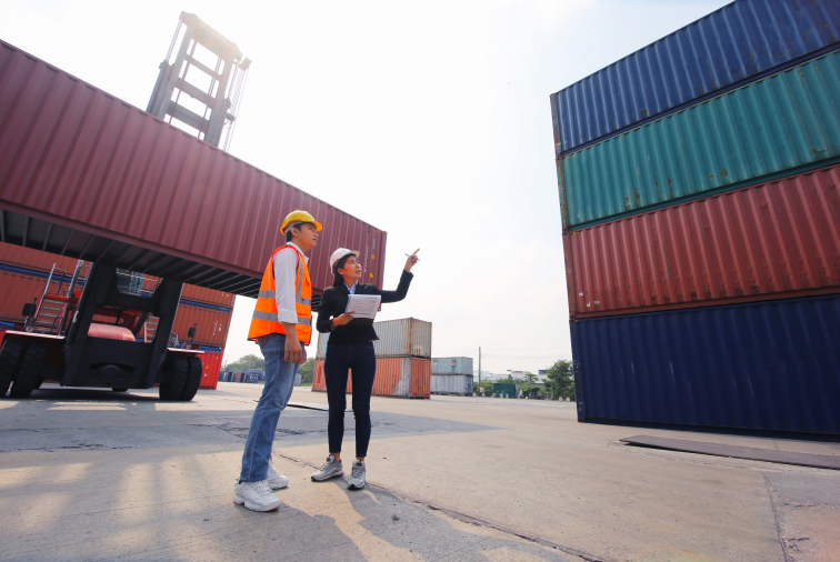 Two persons standing in front of two containers.