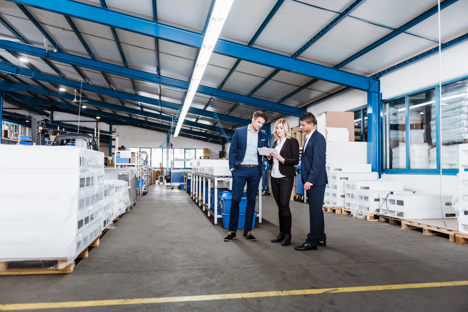 Three business people discussing on shop floor, using digital tablet
