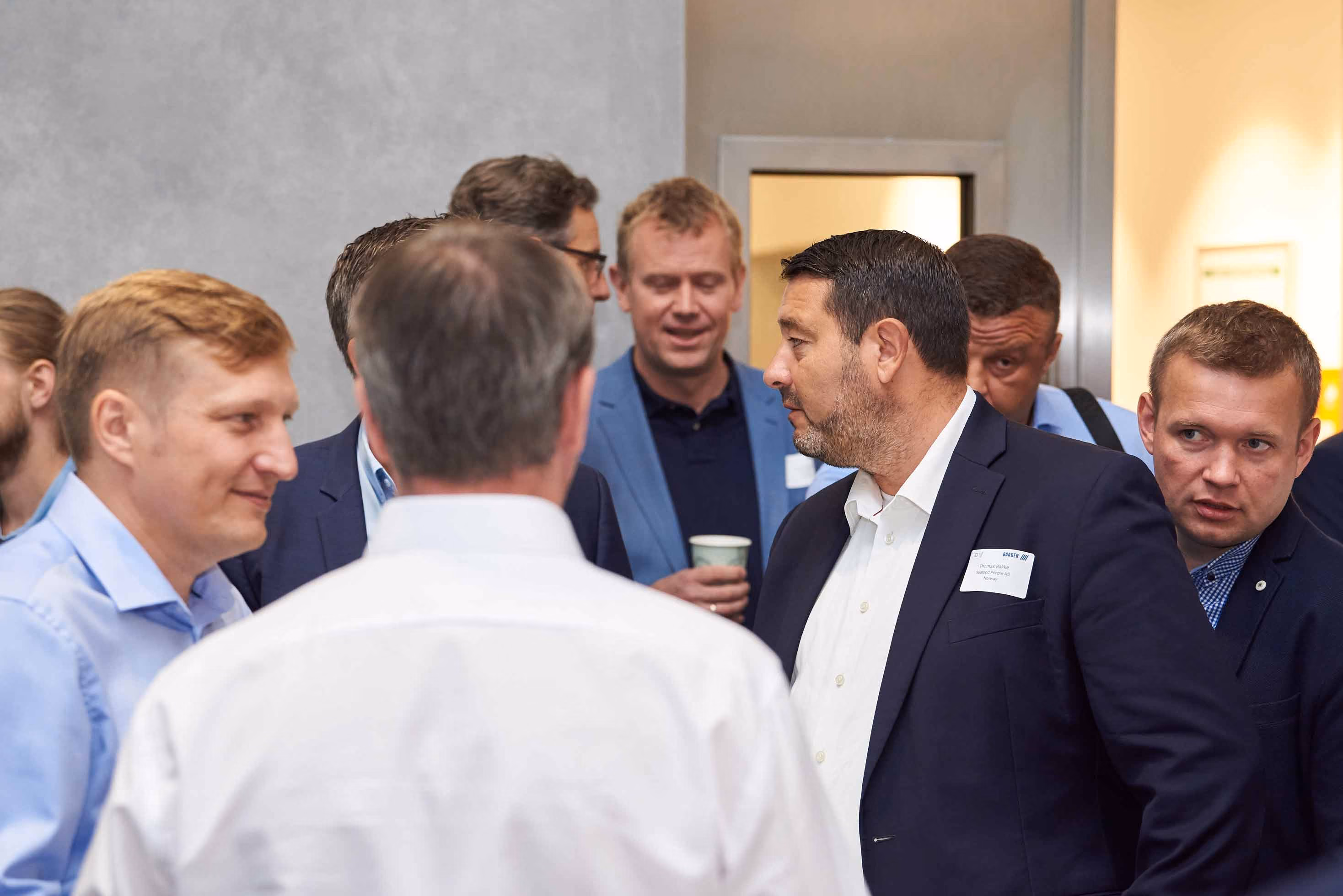 Group of professionally dressed men engaged in conversation at a social or business event indoors.
