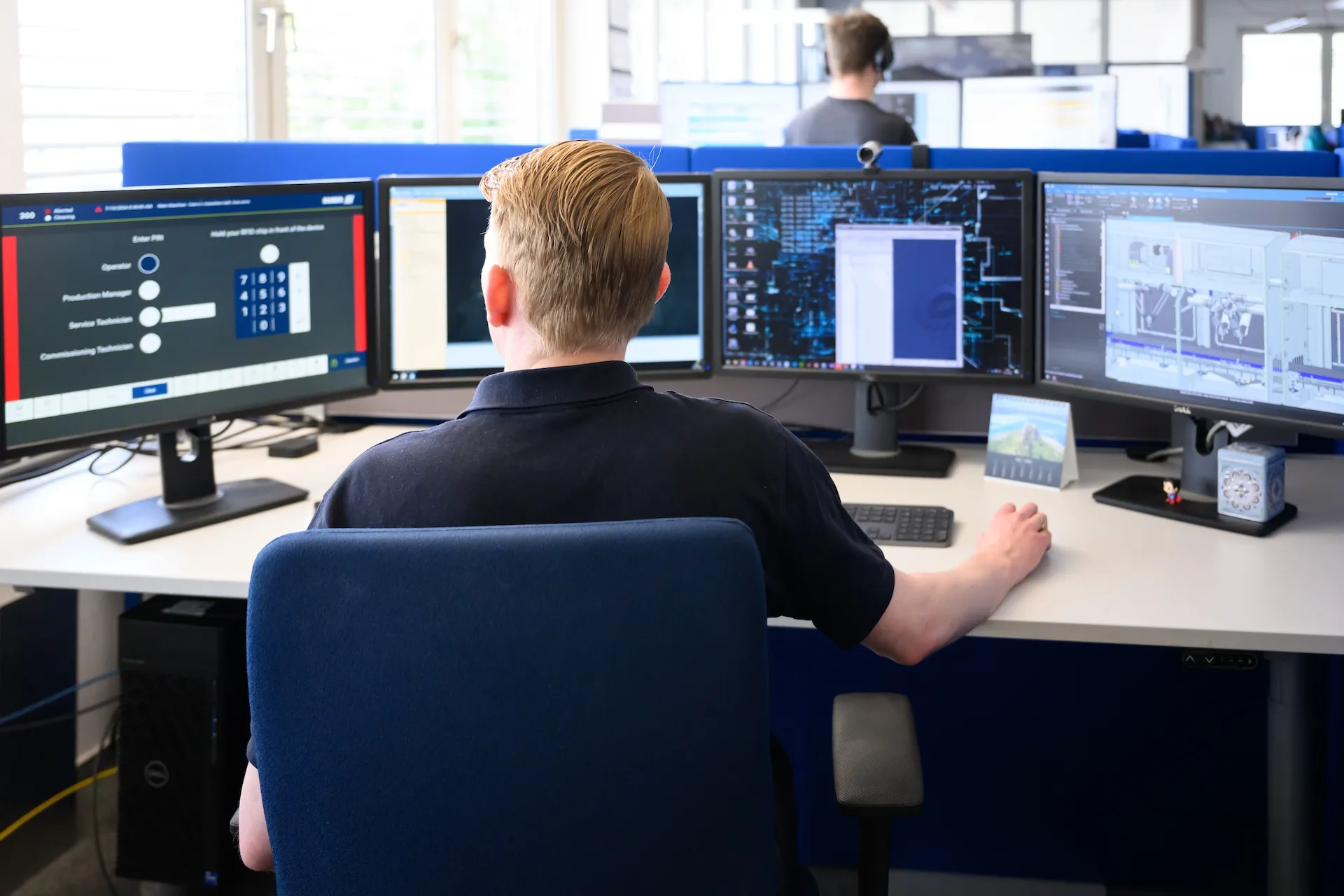 baader employee in front of 3 computer screens working on dashboards