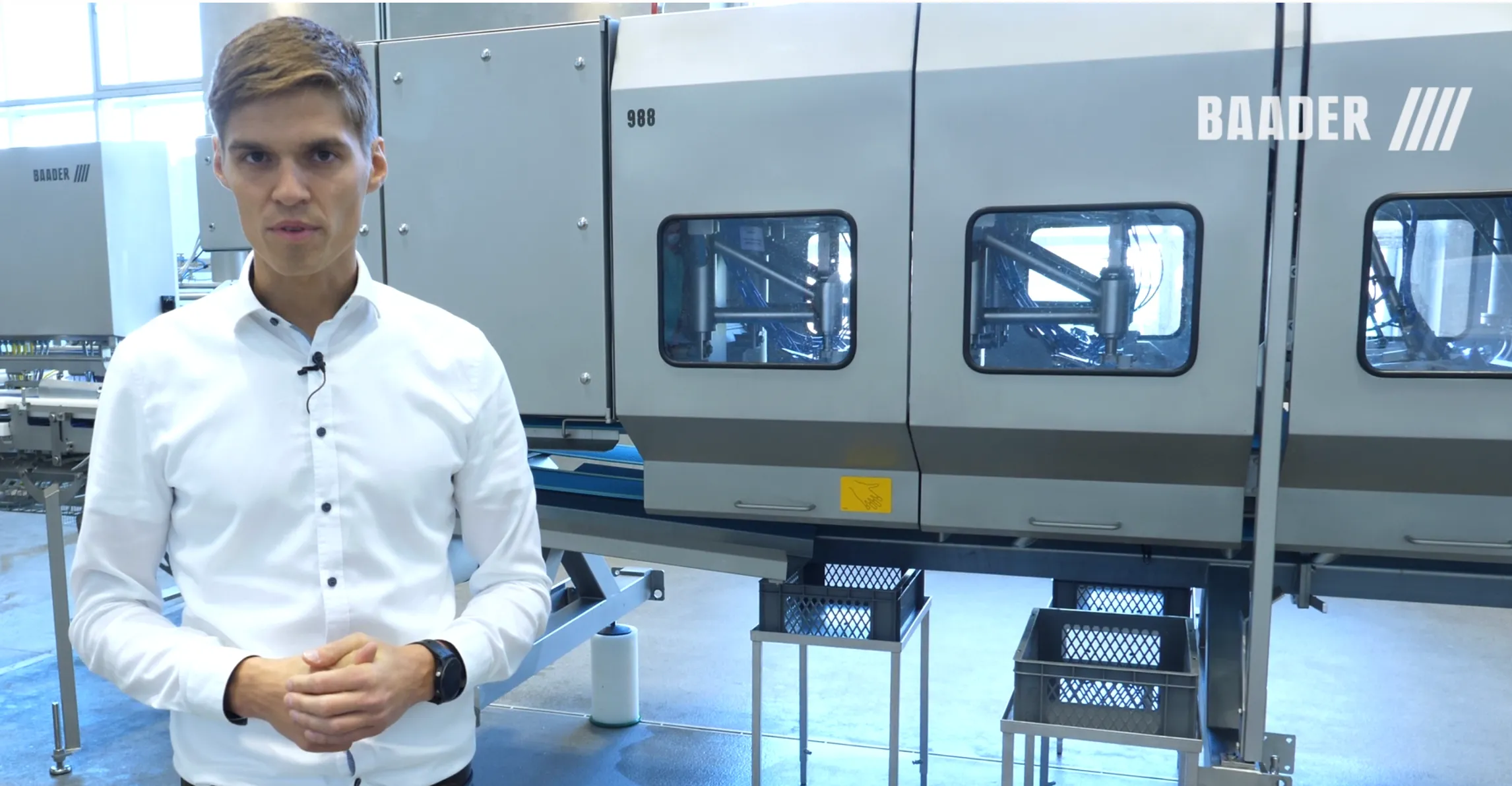 Man in white shirt stands in front of industrial machinery with Baader logo in a manufacturing facility.