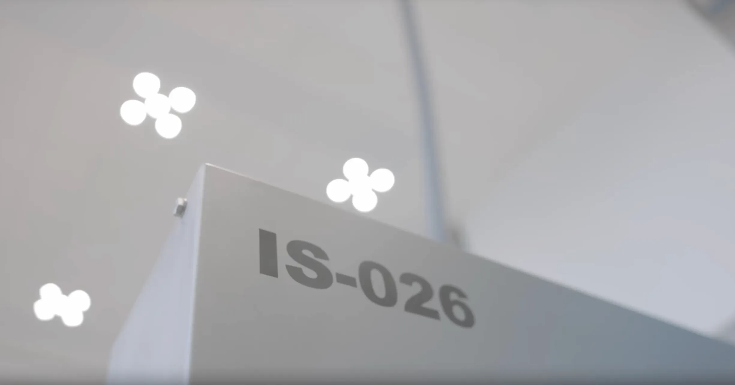 Close-up of a metallic structure edge with the label IS-026 and blurred circular ceiling lights in the background.