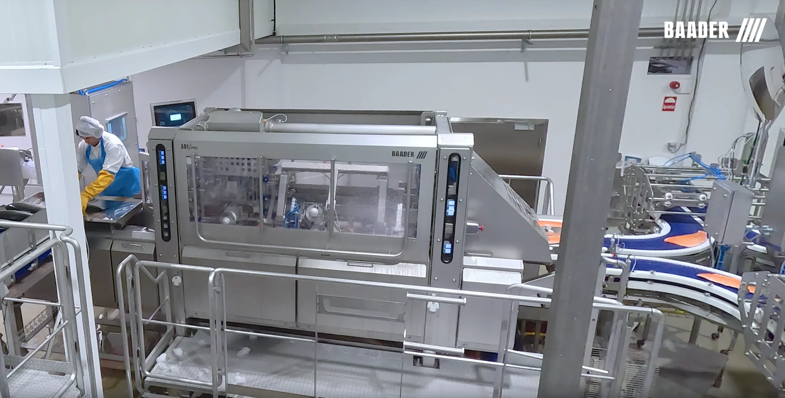 Industrial food processing machine with conveyor belts and a worker in protective clothing operating a tray beside it.