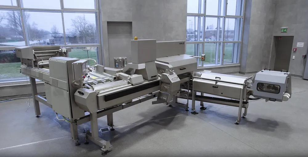 Large stainless steel industrial food processing machine in a factory room with large windows and concrete floor.
