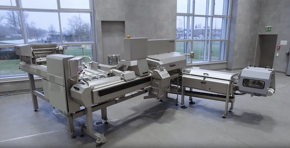 Large industrial food processing machine with multiple compartments and conveyor belts in a spacious room with large windows.