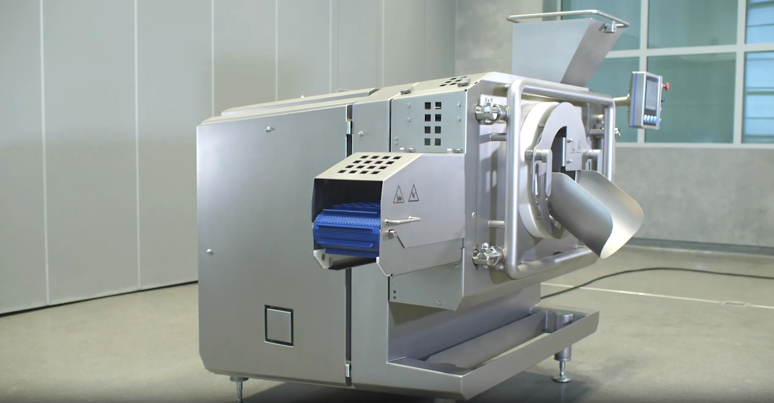 Industrial stainless steel meat processing machine with blue conveyor belt and digital control panel in a clean facility.