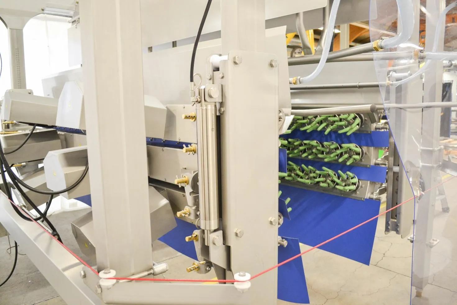 Close-up of industrial machinery with metal parts, green clamps, blue components, and connected cables inside a factory.