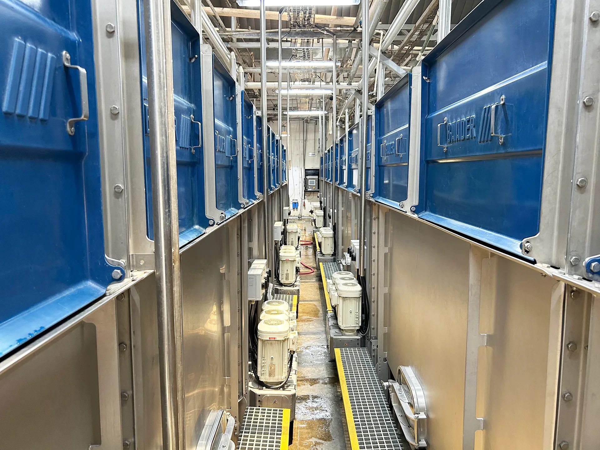 Industrial setup with rows of large metal machines labeled 'CHANDER' and connected motors below, in a narrow corridor.