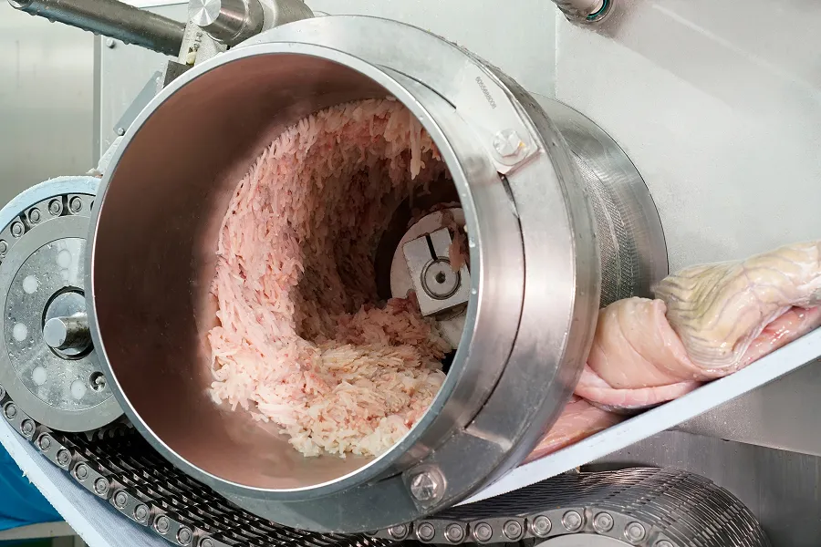 Industrial machine grinding fresh fish into mince on a production line.