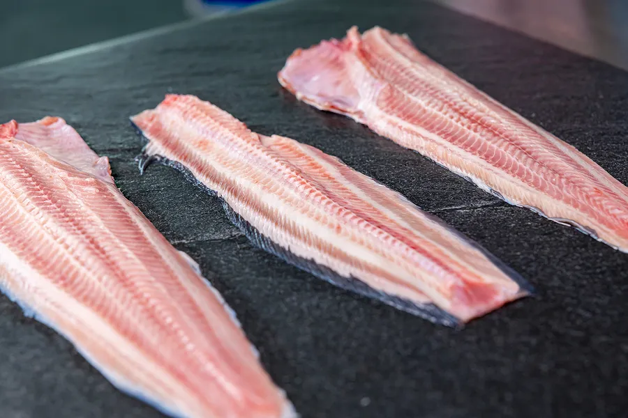 Three raw fillets of African catfish laid out on a black surface.