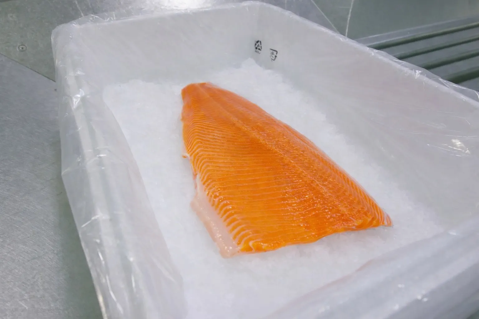 Fresh orange salmon fillet resting on crushed ice inside a white plastic container.