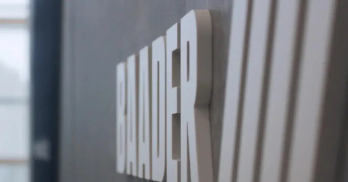 Close-up side view of large white block letters spelling BAUER on a gray wall.