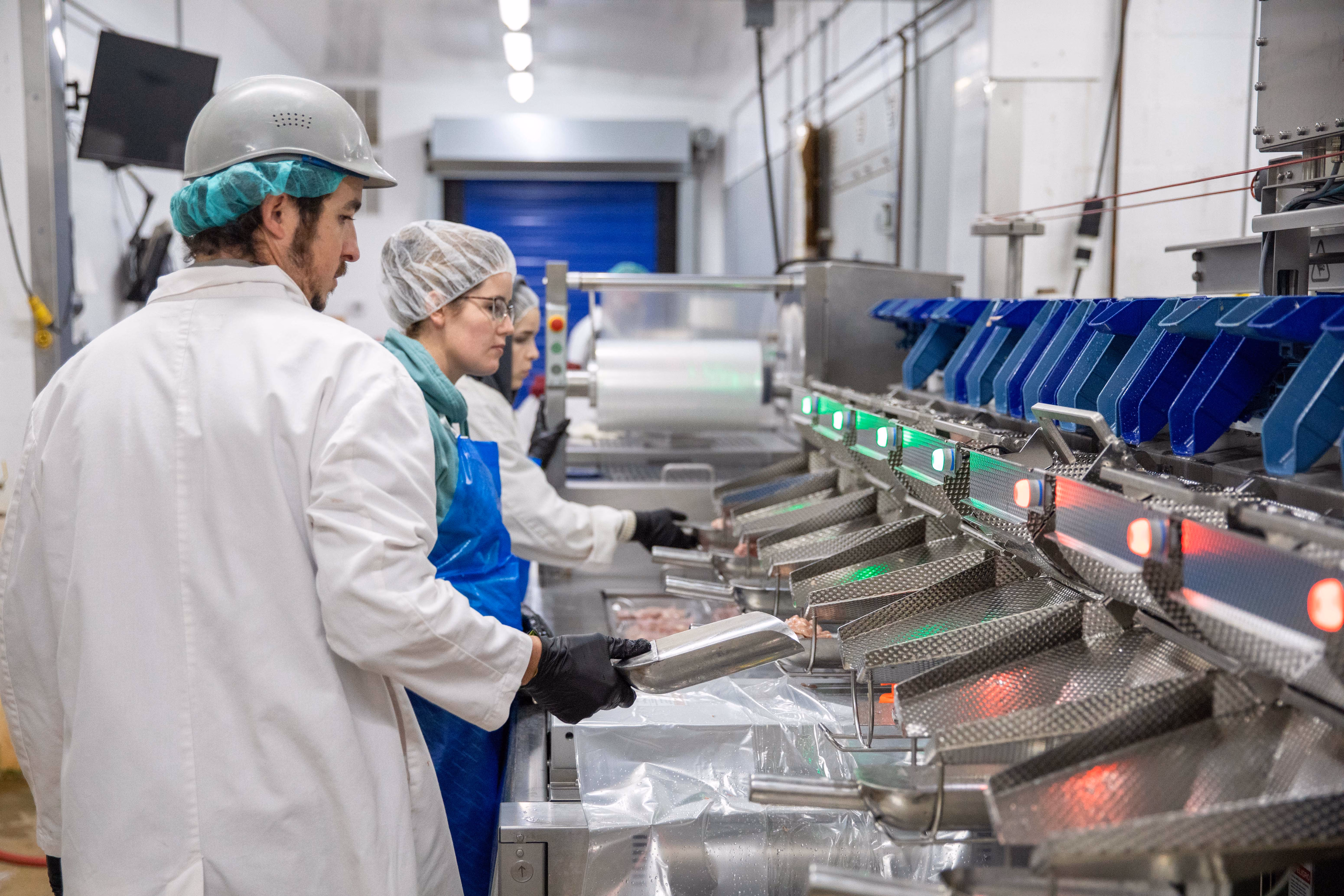 Workers wearing protective clothing sorting poultry meat on a processing line in a food production facility.