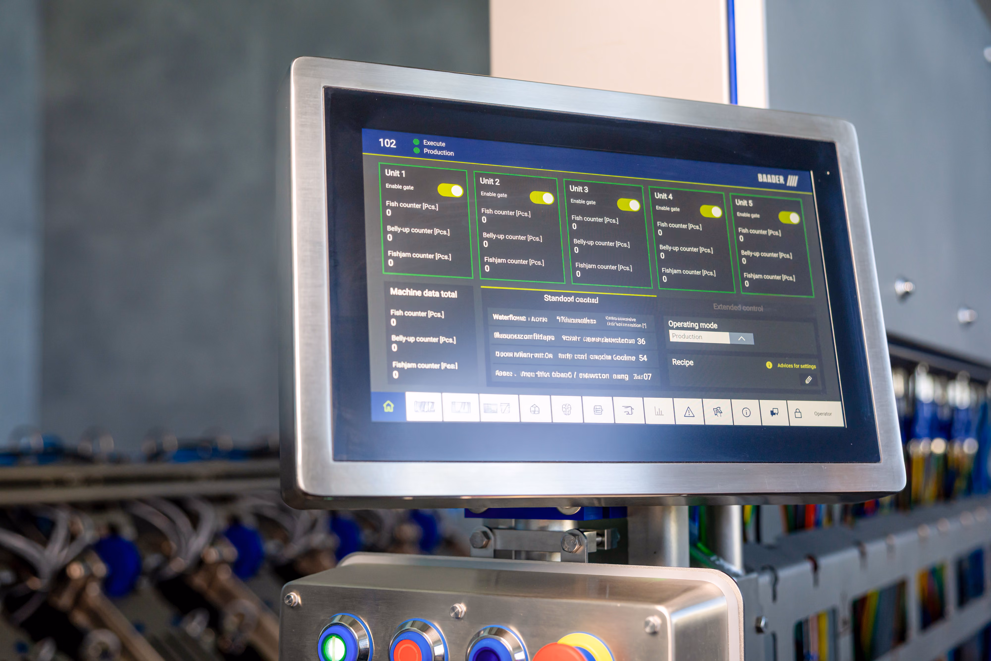 Industrial control panel with a touchscreen display showing unit data and toggle switches above colored control buttons.