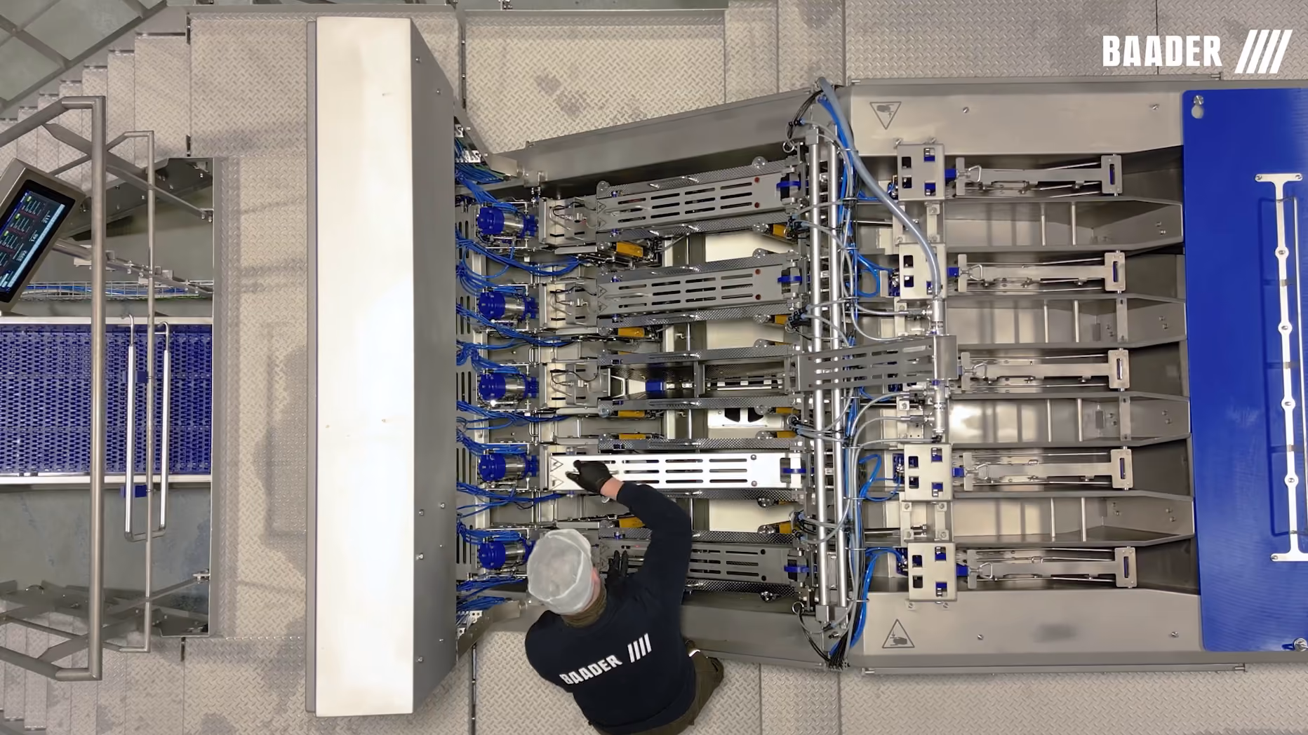 Overhead view of a technician in a Baader uniform performing maintenance on a large industrial sorting machine with multiple metal mechanical arms and blue cables.