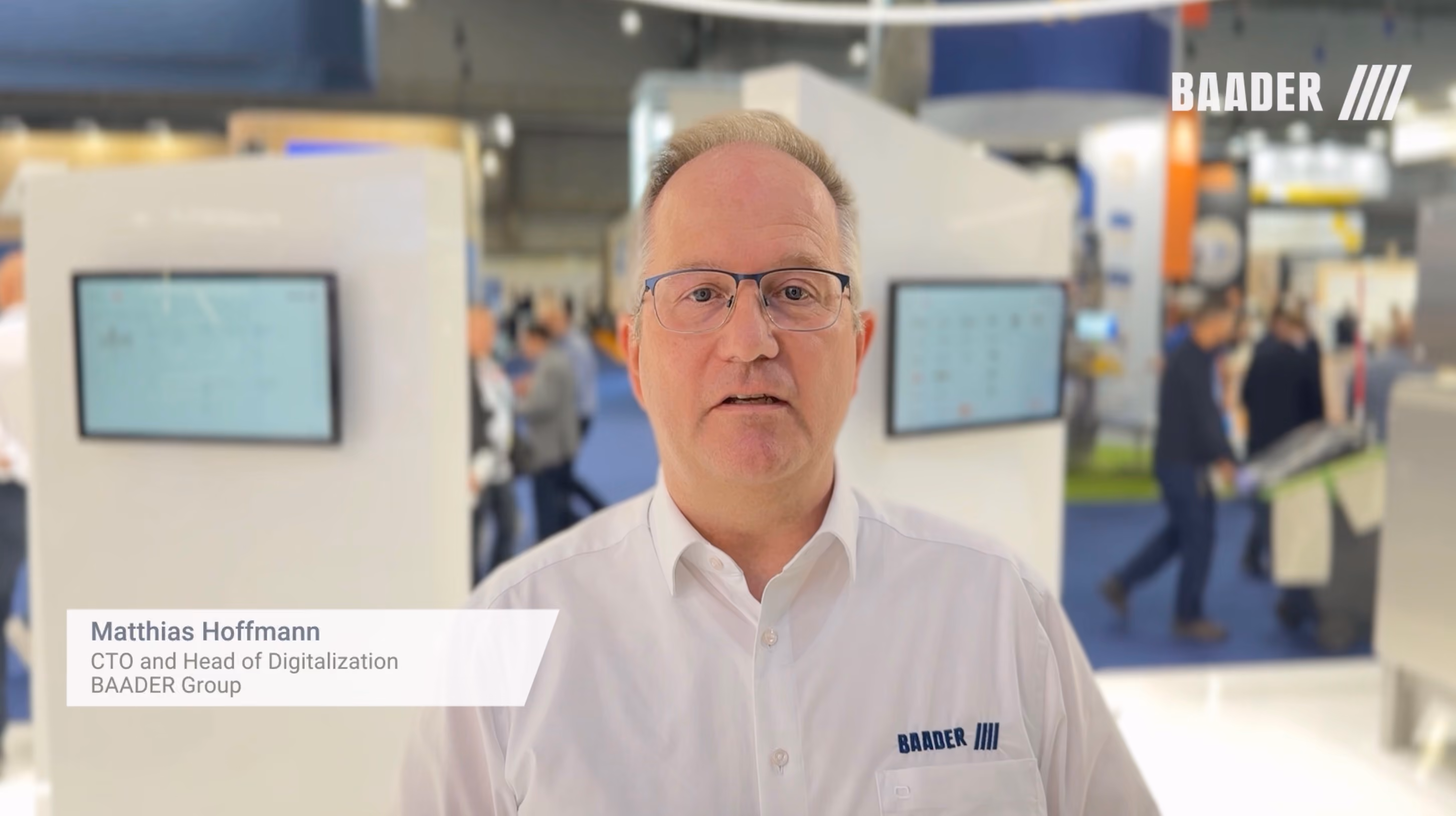 Matthias Hoffmann, CTO and Head of Digitalization at BAADER Group, standing in a trade show booth with monitors and people in the background.