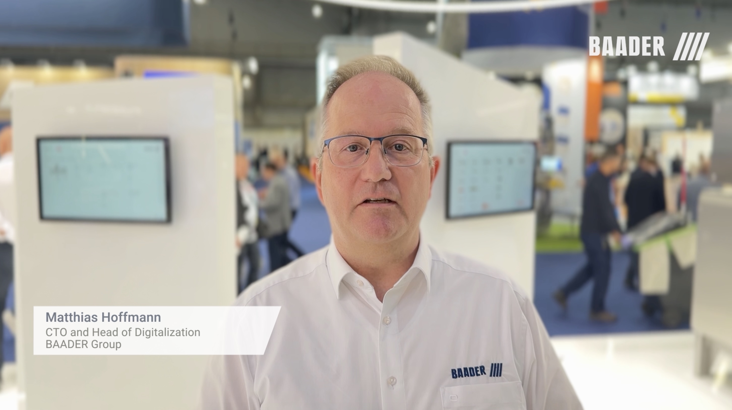 Matthias Hoffmann, CTO and Head of Digitalization at BAADER Group, standing in a trade show booth with monitors and people in the background.