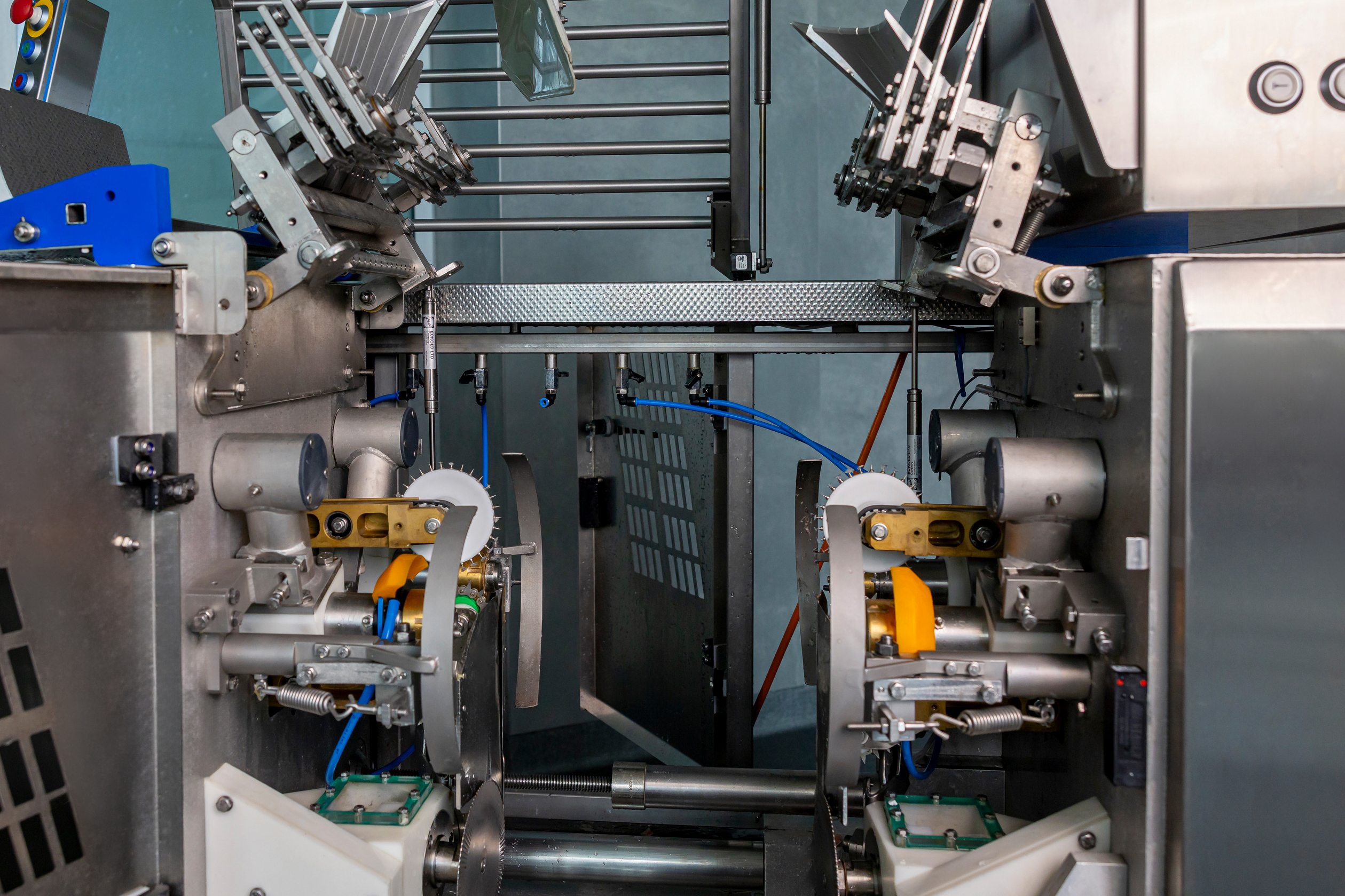 Close-up of an industrial machine with metal parts, gears, and tubes inside a factory setting.