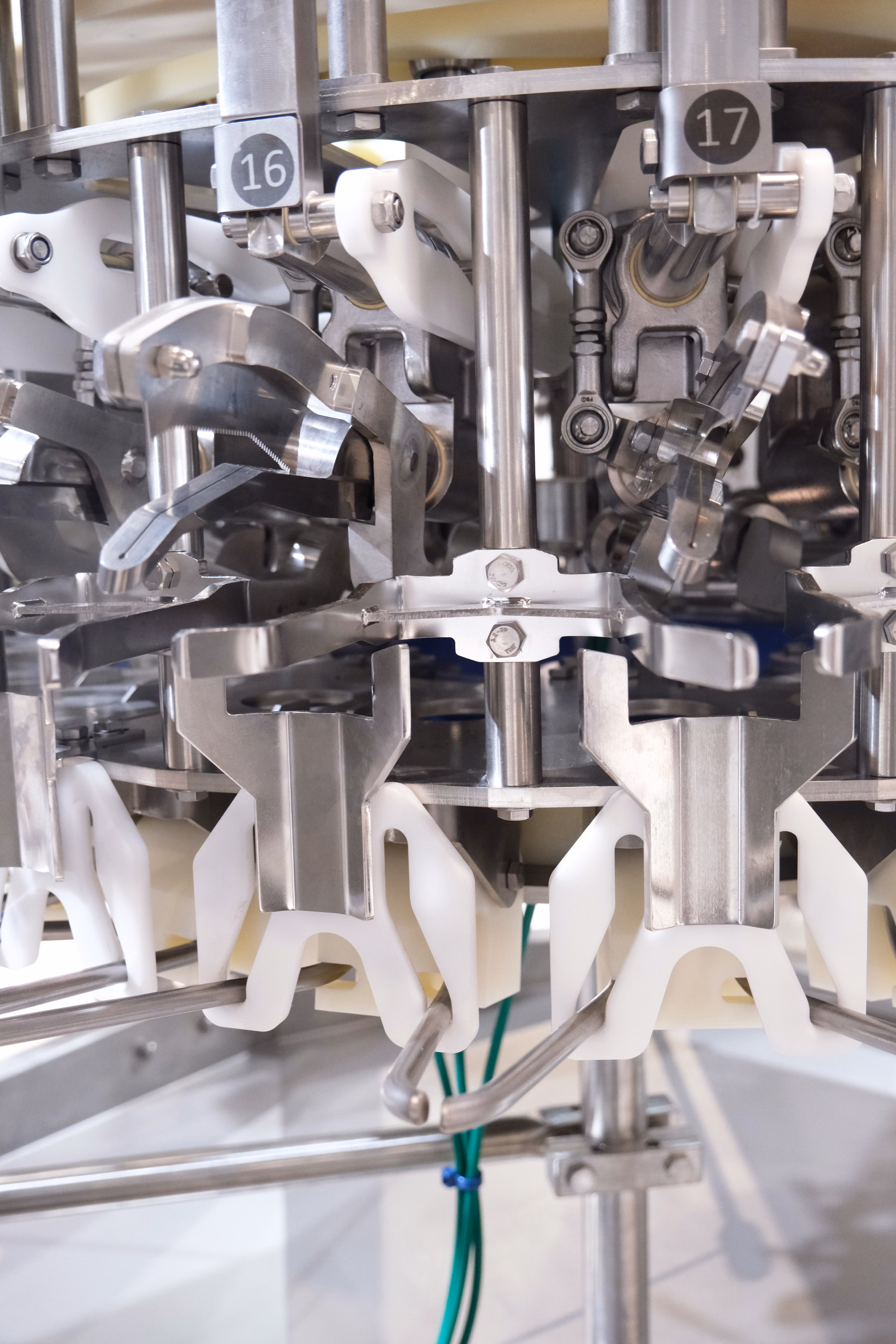 Close-up of a stainless steel and plastic mechanism part of industrial machinery with numbered sections 16 and 17.