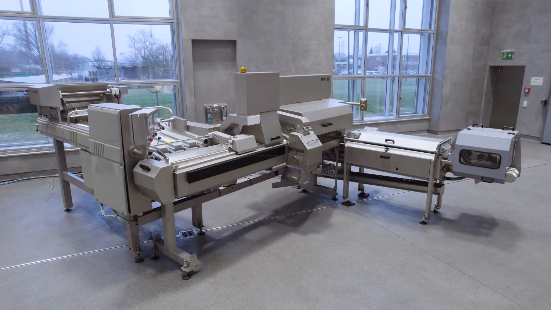Large industrial food processing machine with multiple stainless steel sections in a bright room.