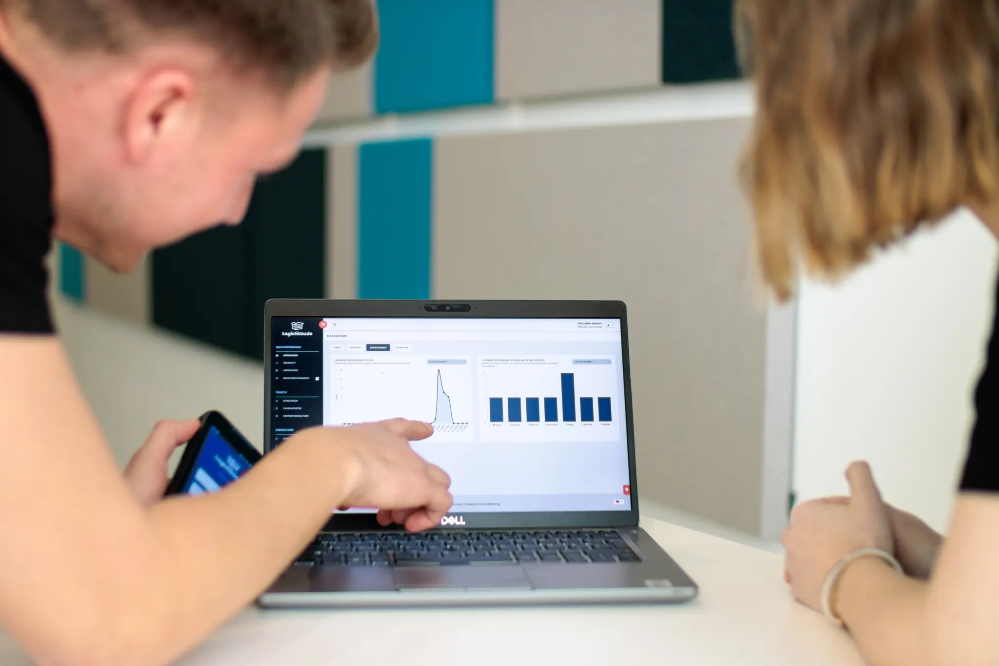 Two people are looking together at the user interface of logistics software on a laptop, on which diagrams and analyses are displayed. One person points to the screen with their finger while the other listens attentively.