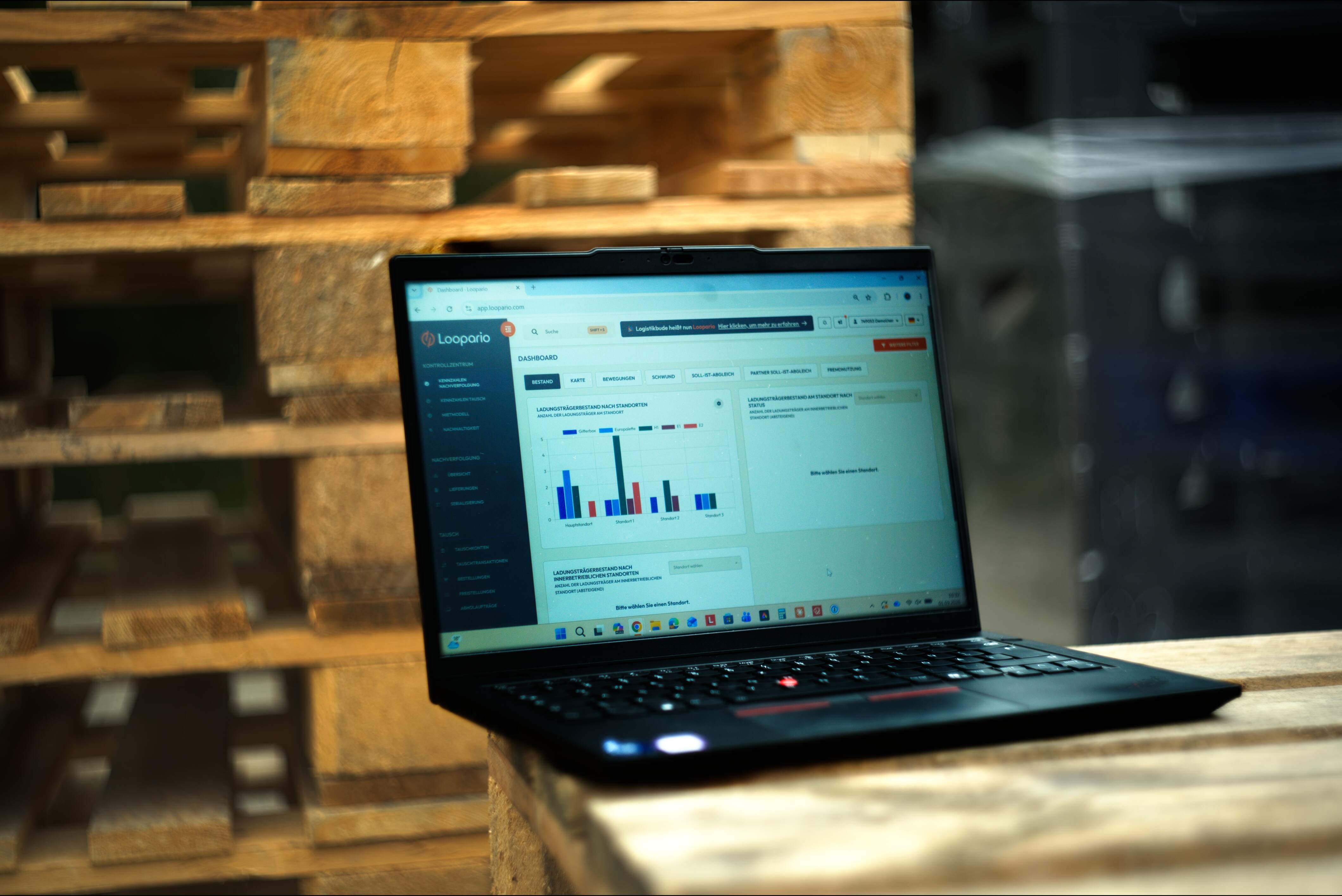 Open laptop on a wooden pallet in a warehouse, showing the Loopario dashboard with bar charts on screen.