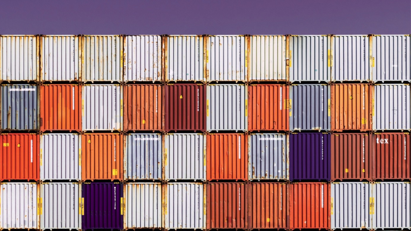 Gestapelte Seecontainer in einem Hafenterminal vor violettem Abendhimmel