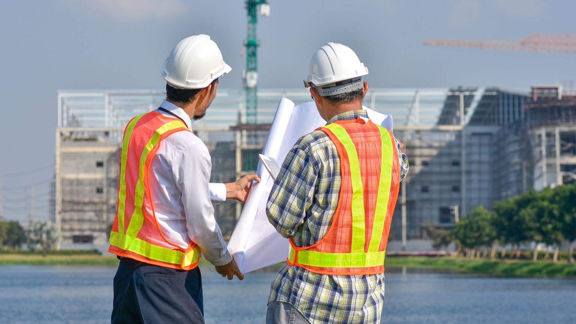 Twee mannen met hesjes aan, bouwhelmen op en bouwtekening voor aanbouw