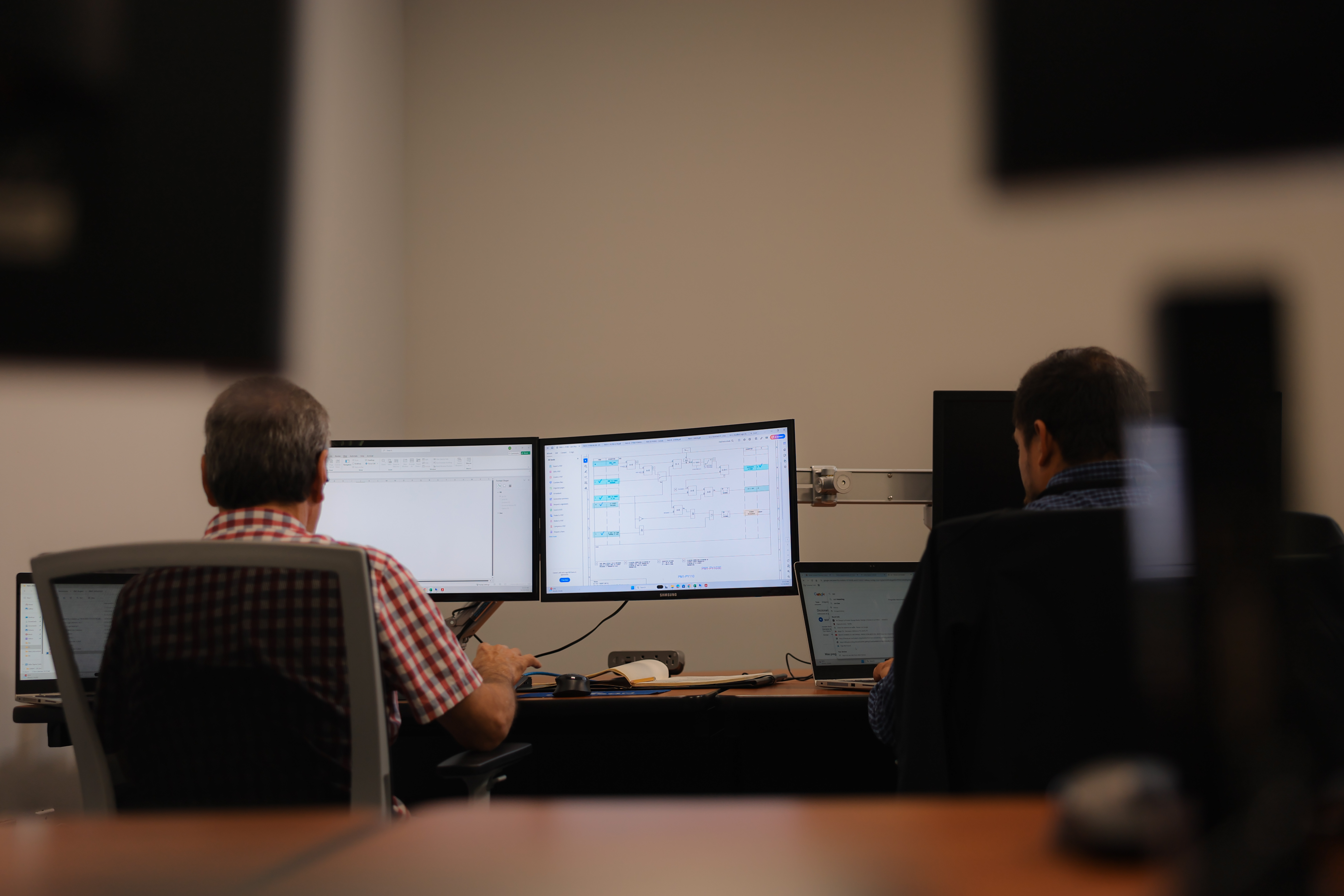 a group of men sitting at a desk with multiple monitors