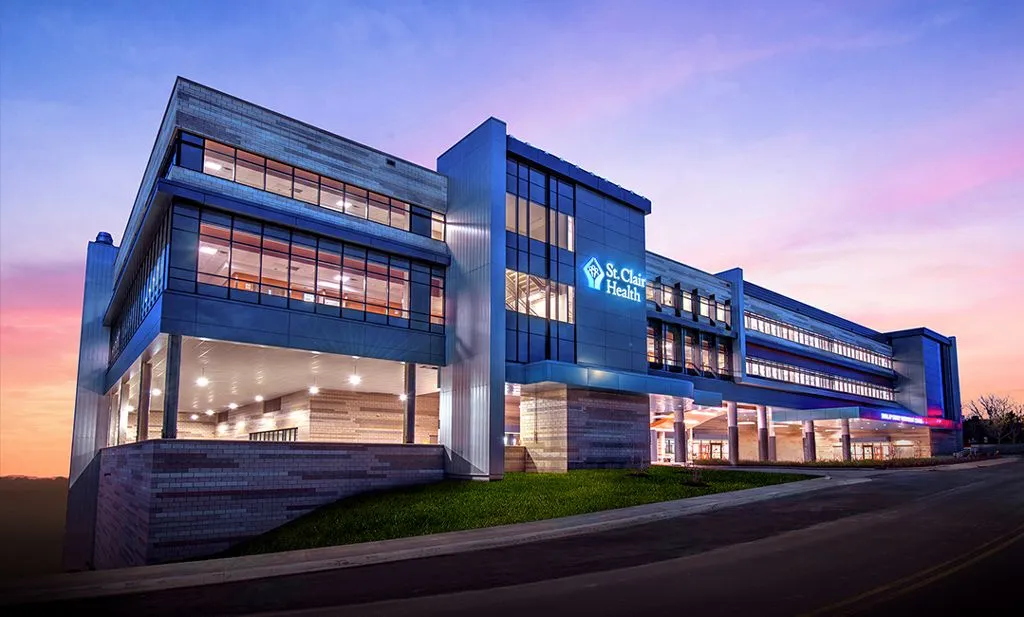 Modern multi-story St. Clair Health medical building at dusk with illuminated windows and a purple and pink sky.