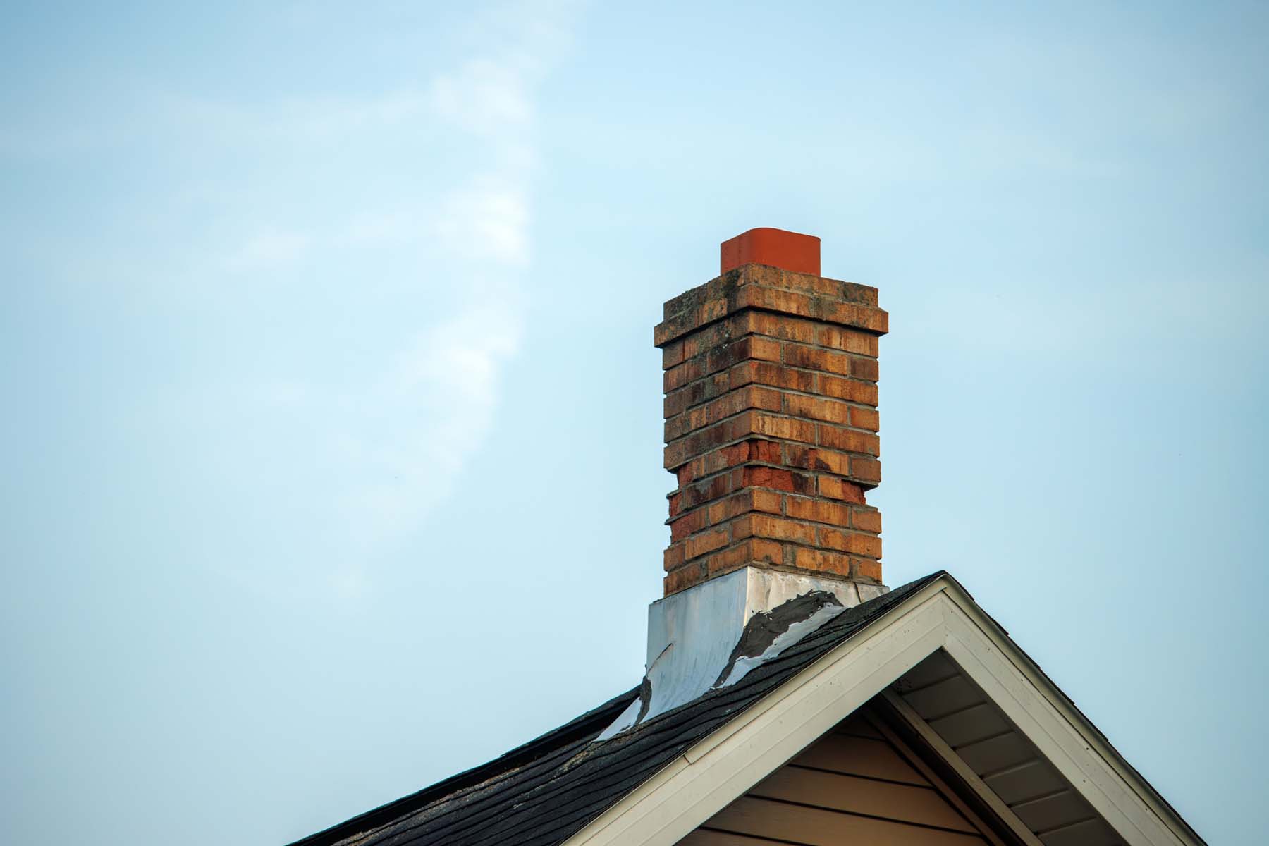 Røykpipe i rød murstein på taket av et hus med blå himmel i bakgrunnen.