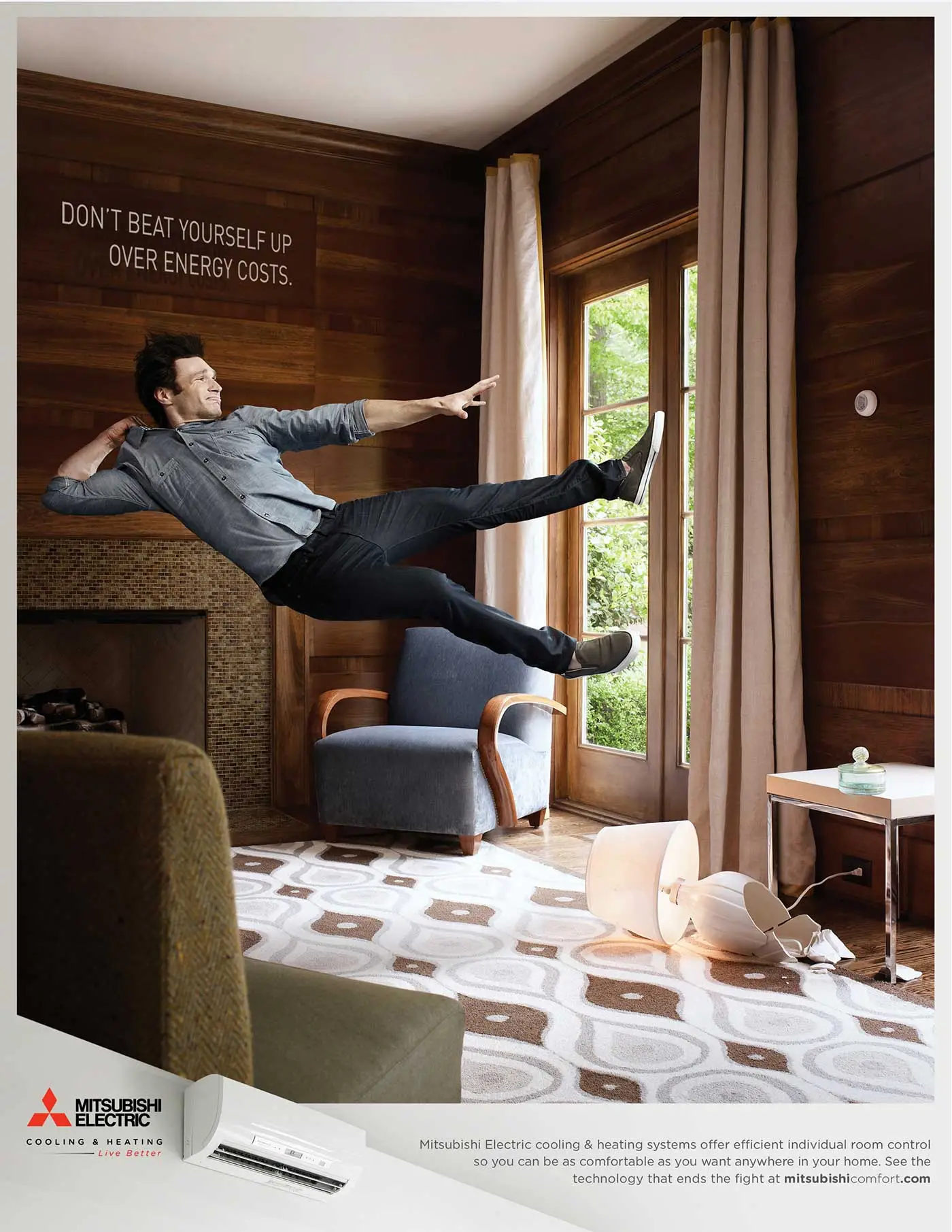 Mitsubishi Electric print ad with man throwing himself across a living room and a headline that reads Don't Beat Yourself Up Over Energy Costs. 