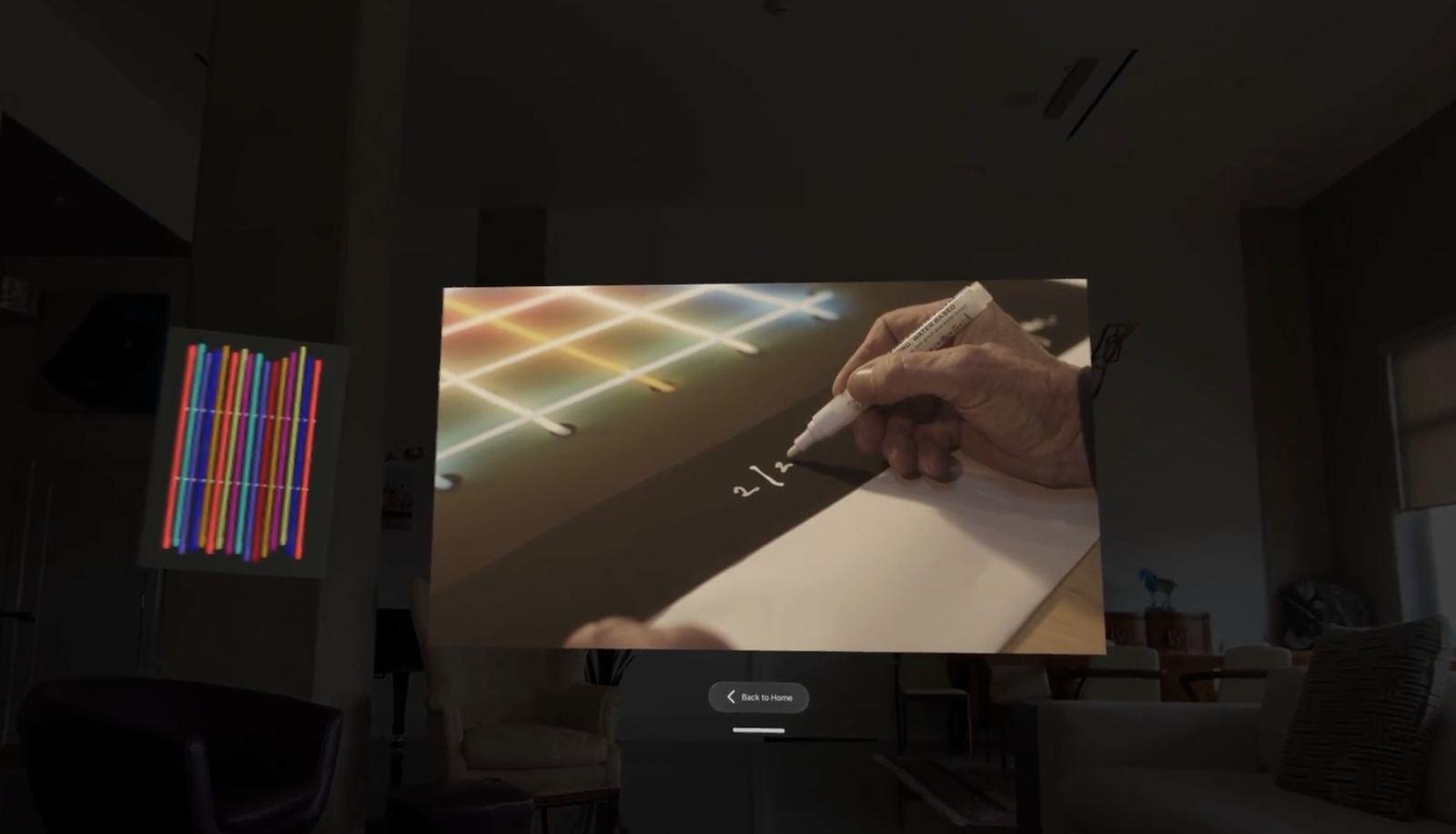 A spatial video panel showing a hand sketching on paper, playing in a dim room next to a shelf of colored pencils.