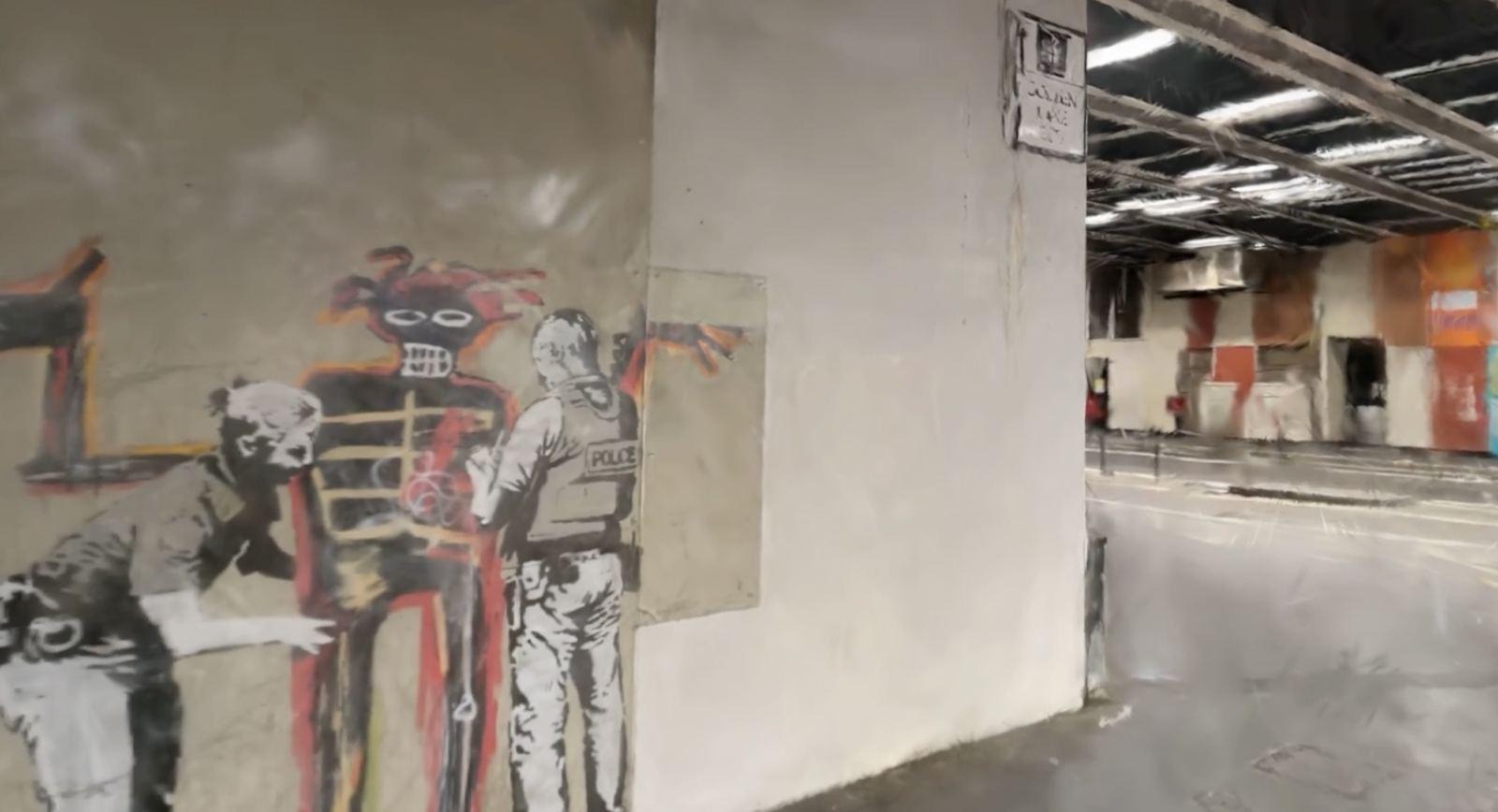 The same mural seen from farther back in a wide industrial hall with a concrete floor and overhead lighting.