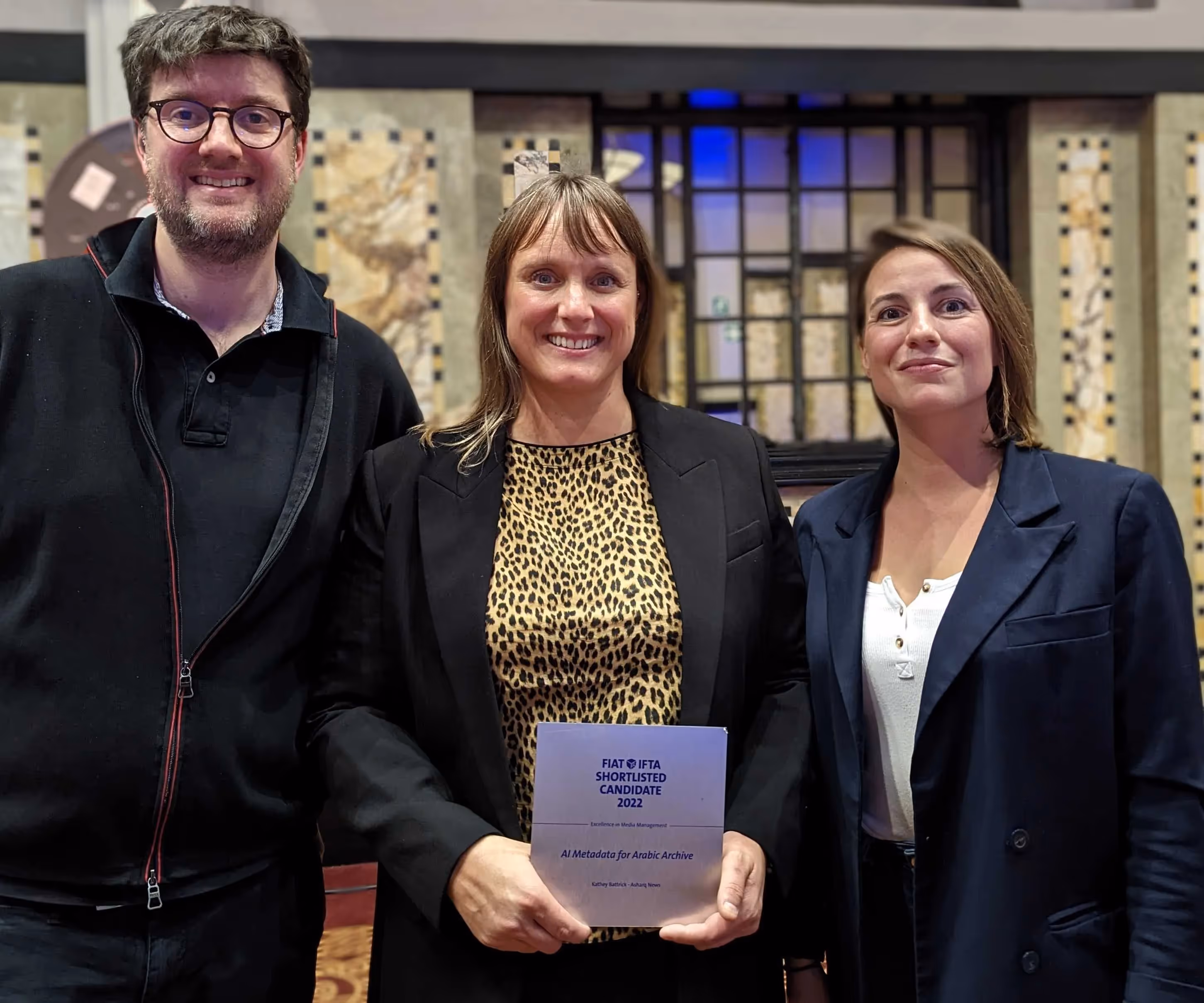 Frederic, Kathey and Carole standing together and smiling for the camera. Kathey is holding a 'shortlisted candidate' sign.
