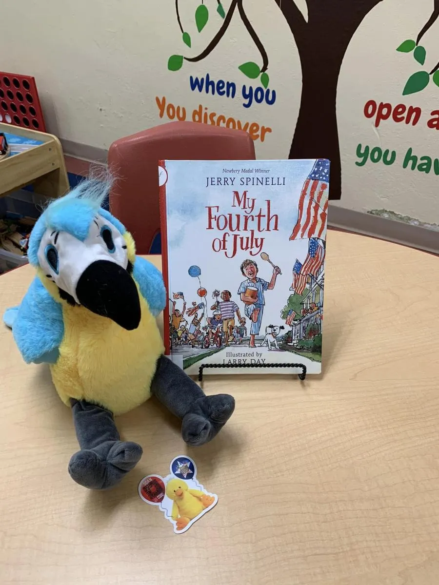A decorative stuffed bird beside a book and a sticker.