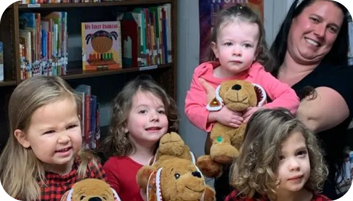 A woman and children holding teddy bears in front of a bookshelf, creating a heartwarming scene.