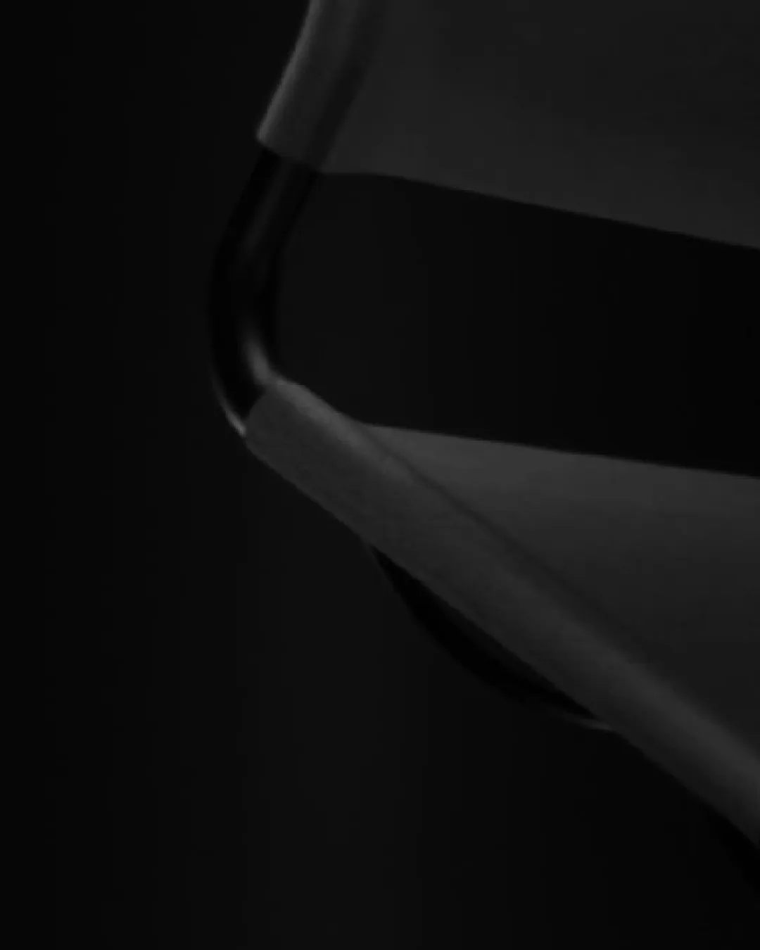 Close-up of a black metal frame with a dark fabric stretched over it against a black background.