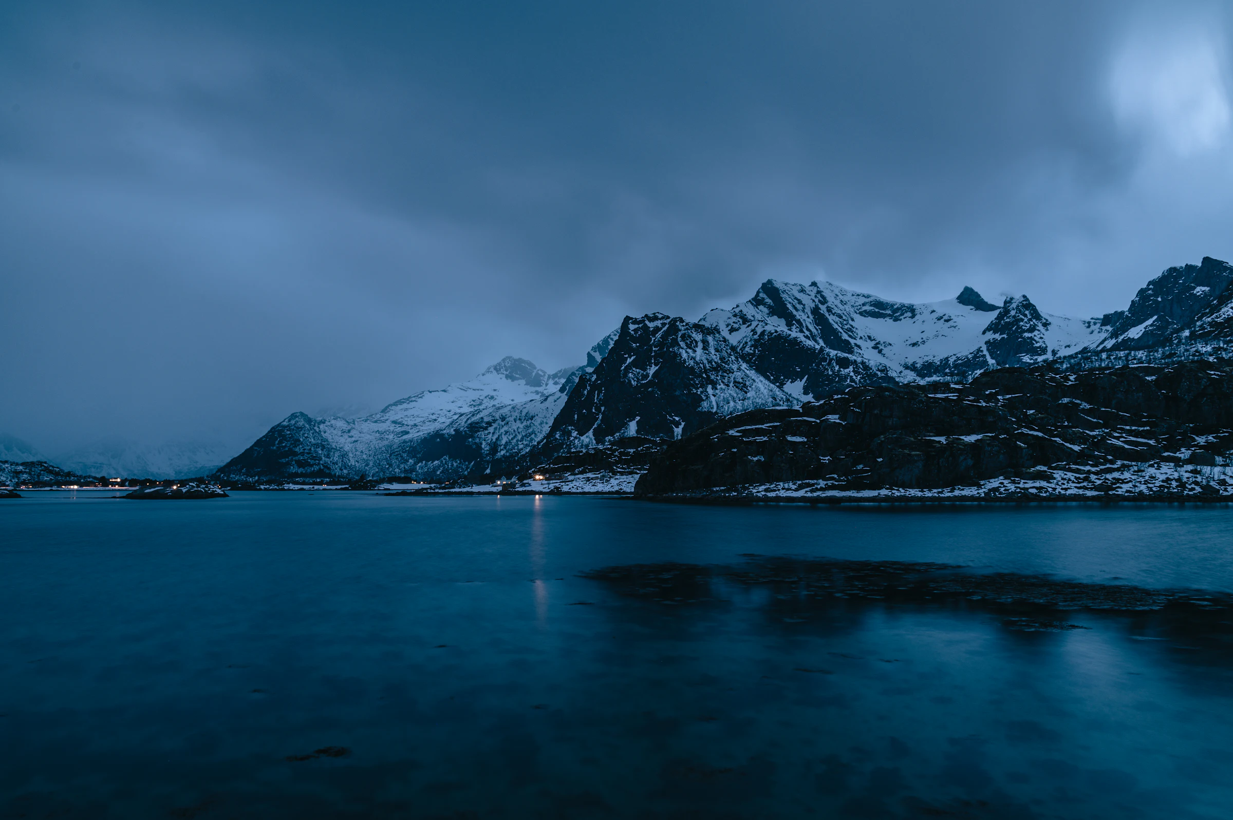 Snow-covered peaks above a still fjord in Lofoten, Northern Norway, at blue hour