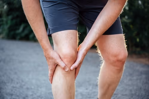 bildet viser en mann i treningsshorts som holder seg til patellasenen som fester seg på tibia (leggbenet) rett nedenfor kneskålen, og indikerer at han kanskje har patellartendinopati, hopperkne, jumper's knee.