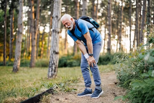 bildet viser en eldre mann på tur i skogen som holder seg til beinet i smerter på grunn av nevrogen claudicatio som følge av lateral recess stenose i ryggen.