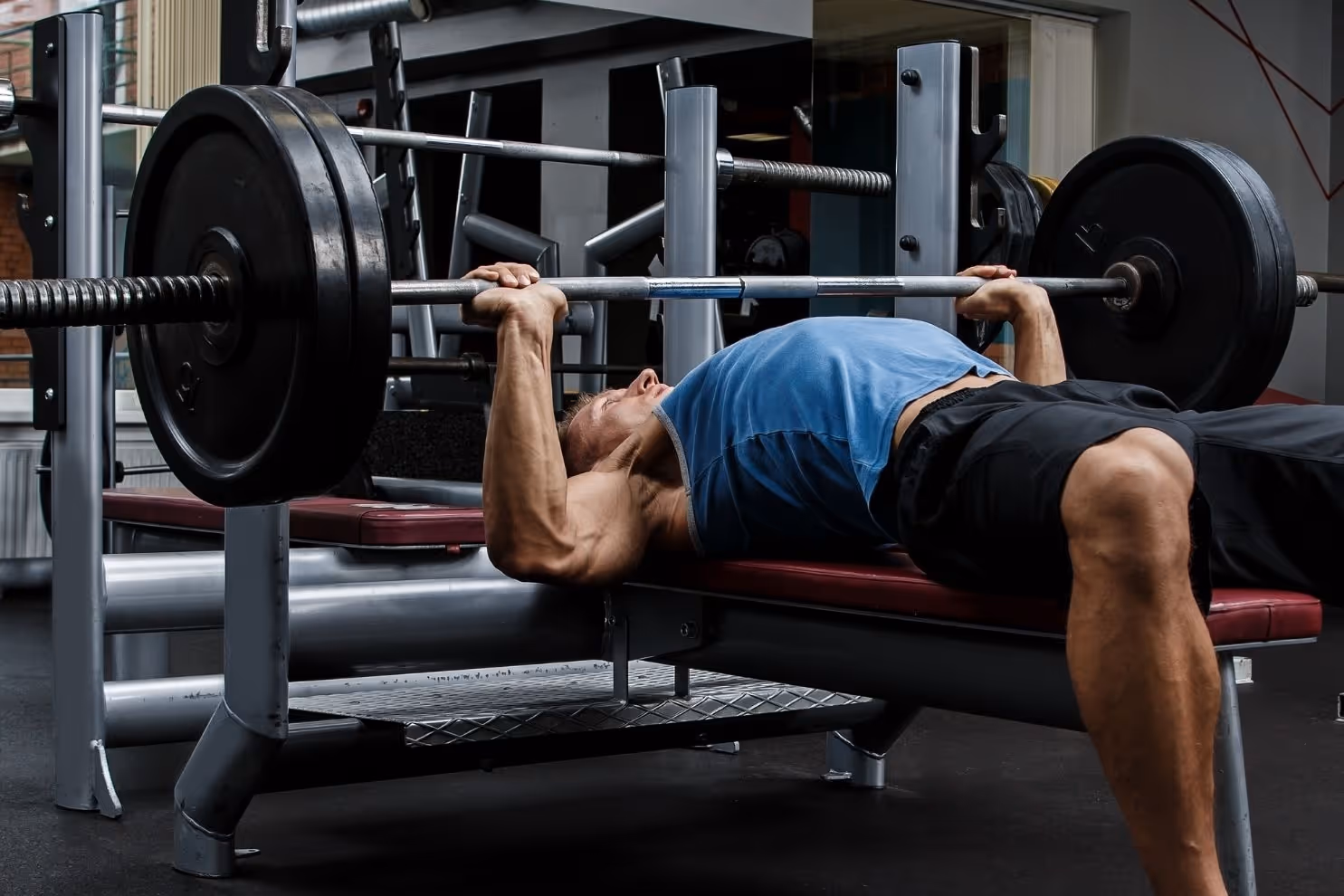 bildet viser en ung muskuløs mann som ligger på et benkpressapparat og løfter benkpress. Bildet viser en typisk aktivitet som belaster acromioklavikular leddet mye, og en typisk årsak til AC-ledds smerter relatert til forstuing av AC-leddet.