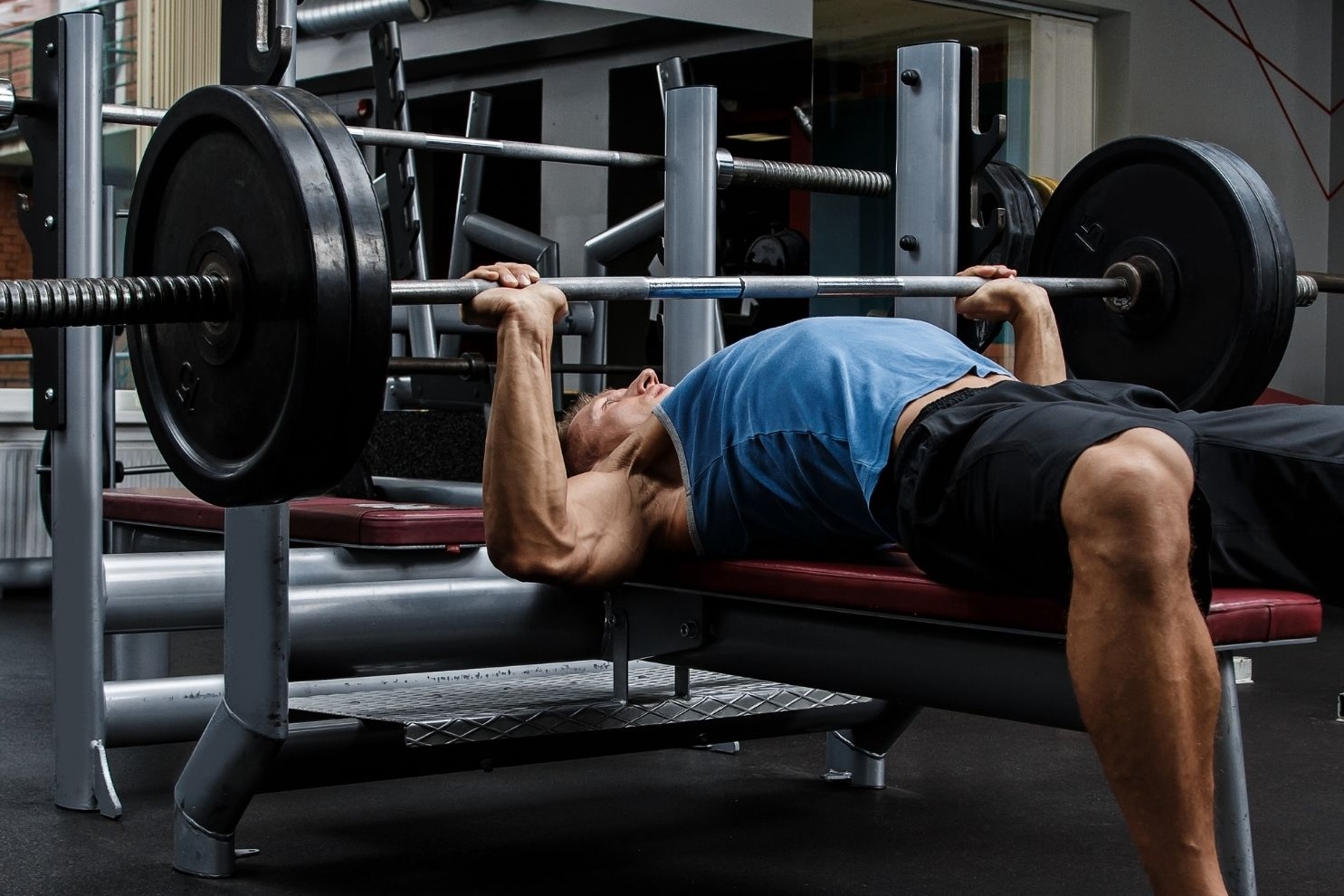 bildet viser en ung muskuløs mann som ligger på et benkpressapparat og løfter benkpress. Bildet viser en typisk aktivitet som belaster acromioklavikular leddet mye, og en typisk årsak til AC-ledds smerter relatert til forstuing av AC-leddet.