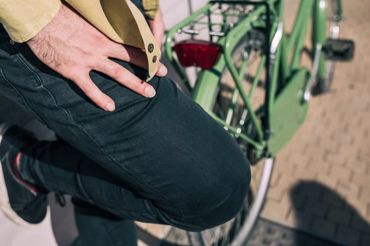 bildet viser en kvinne som sitter på sofaen med bøyd kne og holder seg til bakside legg, muligens på grunn av strålesmerter fra ryggen grunnet isjias. 