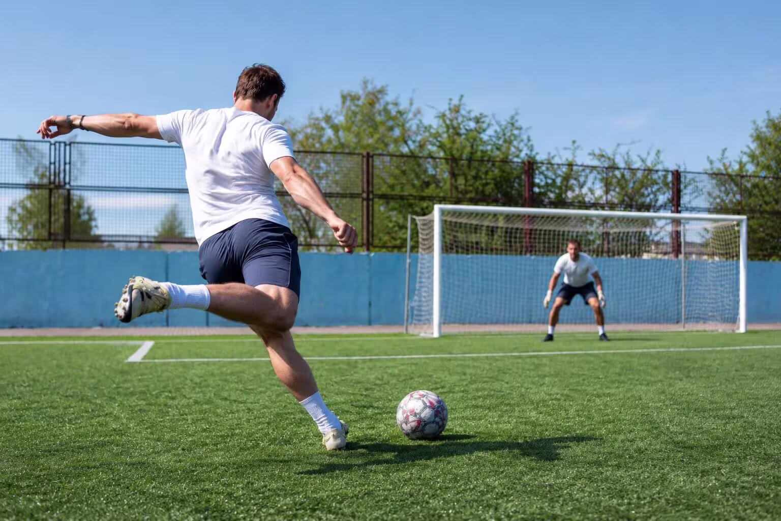 Fotballspiller sett bakfra i ferd med å sparke ballen mot mål, med benet svingt bakover – illustrasjon av spark, en vanlig årsak til lyskestrekk (strekk i adduktorene på innsiden av låret)