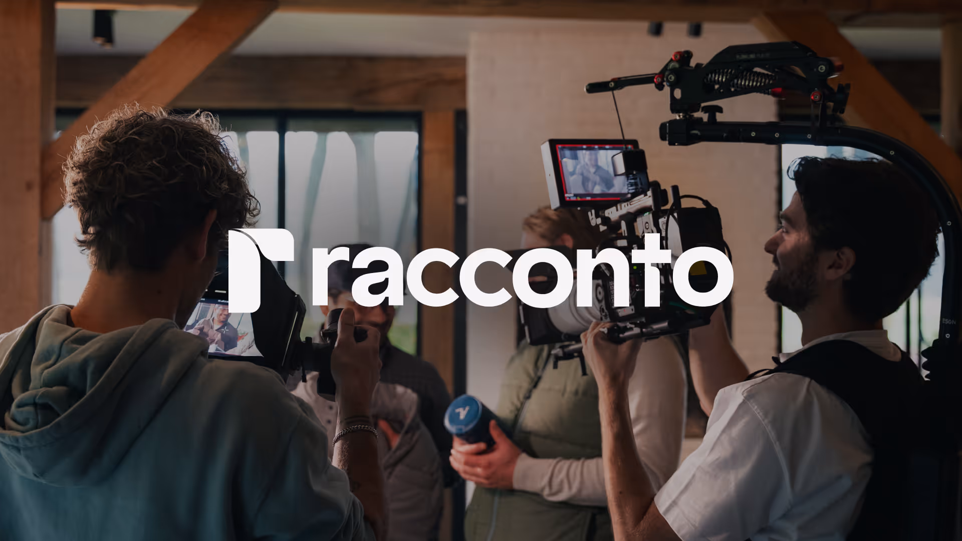 Racconto logo on an image of two men filming a person holding a blue water bottle inside a room with wooden beams and windows.