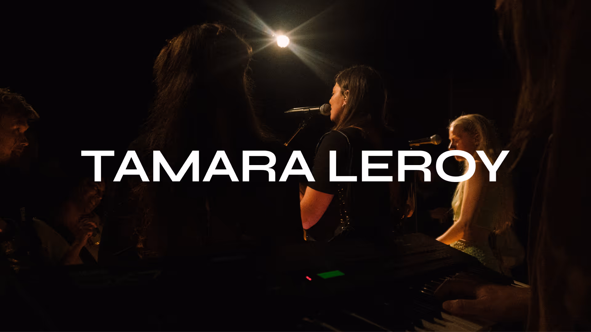 Tamara Leroy logo on a picture of side view of a woman singing into a microphone on stage with a bright spotlight behind her.